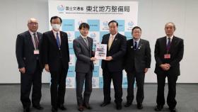 東北地方整備局内の国土交通省東北地方整備局と書かれたボードの前で梅野修一局長に道路の整備促進の要望書を渡しているところに同行した市長を含めた岩手県道路整備促進期成同盟会10団体の方も並んで6人で撮影した写真