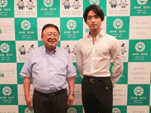 バックパネルの前で身体の後ろで両手を組む太田倫功さんと市長が横並びで写っている写真