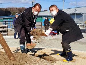 長靴を履いた市長と関係者の男性がショベルを持って土を掛けている瞬間の写真
