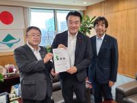 観葉植物や応接セットが設置された室内で、環境省の大岡敏孝副大臣と市長が要望書を一緒に持ち、宮古市議会の橋本久夫議長と横一列に並んでいる写真
