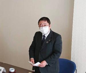紺色の椅子を後ろに引き、お腹の前で資料を両手で持ち立って話している様子のマスクを着けた市長の写真