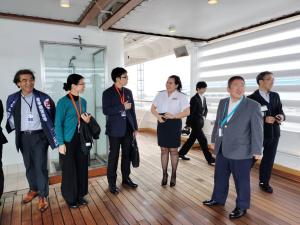 市長と関係者の方々が船内見学している中、男性が女性の乗務員と話をしている写真