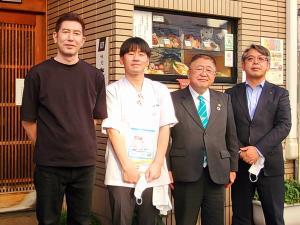 飲食店の食品サンプルが並んだショーケースの前で横並びになって写る市長と男性3人の写真