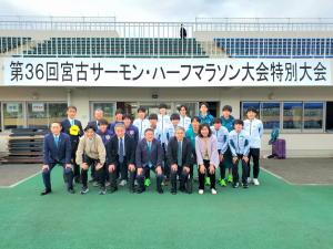 陸上競技場の観覧席に「第36回宮古サーモン・ハーフマラソン大会特別大会」と書かれた横断幕が貼られた前で、市長を中央にゲストランナーや関係者が3列に並んでいる記念写真