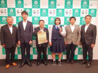 バックパネルの前で市長が賞状を手に持ち、舘下苺采(いちね)さんと関係者4名が並んでいる写真
