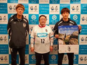 いわてグルージャ盛岡のユニフォームを着た市長が中村太亮選手と試合のポスターを持った加賀美登生選手と並んで撮影した写真