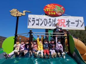 ドラゴンひろば祝オープンと書かれた幕がかかった、すべり台で市長と8人の子供たちが集合して撮影した写真