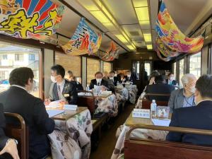 窓の上には大漁旗が飾られ、座席がこたつ形式になっているお座敷列車に参加している皆さんを撮影した写真