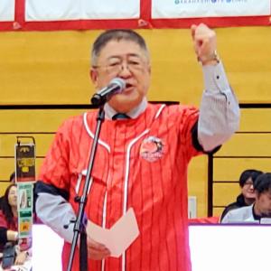 岩手ビッグブルズの応援シャツを着た市長がマイクの前で左こぶしを突き上げ挨拶をしている写真