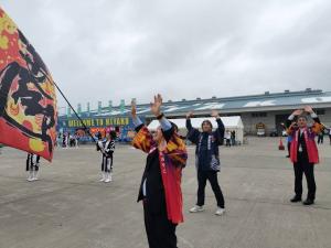 客船に向かって両手を上げて手を振る市長や手を振ったり、大きな旗を振ったりしている関係者の方々が写った写真