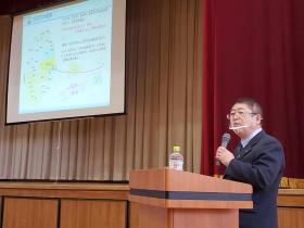 高校の体育館で、市長がスクリーンに映し出された岩手県の地図を見ながらステージ下の演台で宮古市の取り組みやこれからのまちづくりについて話している写真