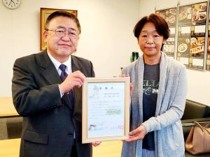 賞状の額縁を一緒に持った市長と女性が並んで立っている写真