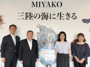 「MIYAKO 三陸の海に生きる」という文字と絵が描かれた壁の前で横一列に並んで記念撮影をする市長、関係者の男性1名、女性2名の写真