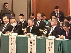 出席者が長机に並んで席についている会場で、マイクを持ち意見発表をする市長の写真
