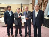 国旗が置かれた室内で、財務省の鈴木俊一大臣と市長が要望書を一緒に持ち、宮古市議会の橋本久夫議長と宮古商工会議所の大坂文人副会頭が横一列に並んでいる写真