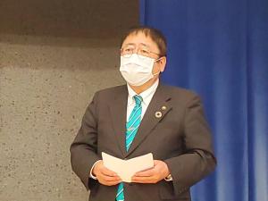 お腹の前で両手で持った資料を広げ、前を向いて話をしている様子の市長の写真