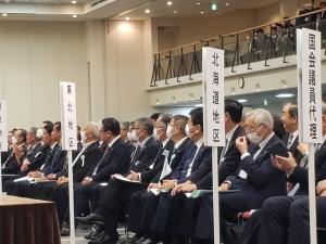 各地区ごとに分かれて大勢の出席者が座っている会場の様子の写真