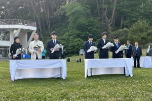 献花台の前で白い花束を持ち立つ女性1人、男性5人の写真