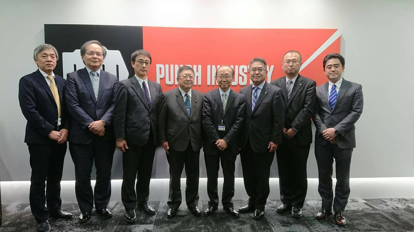 パンチ工業株式会社のロゴマークが表示された壁の前で、武田雅亮代表取締役社長と他3名のご担当者に市長と副市長、2名の関係者の男性が横一列に並んでいる写真