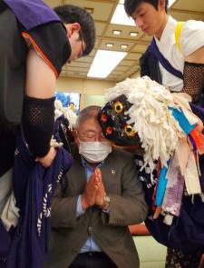 市長が目を閉じて手を合わせている状態で、黒い獅子舞に頭を噛んでもらっている写真