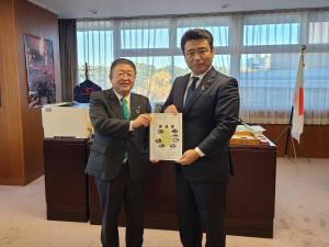 国旗が設置された執務室内で、国土交通省の西田昭二大臣政務官と市長が一緒に要望書を持ち並んでいる写真