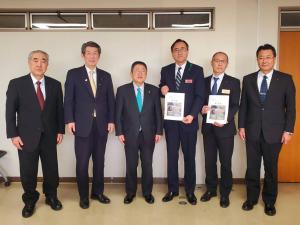 6名のスーツ姿の男性が1列に並び、右から2番目と3番目の男性が要望書を持っている写真