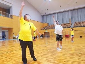 体育館のフロアで右手を上に、左手を斜め下に下げてポーズをとる市長と参加者たちの写真