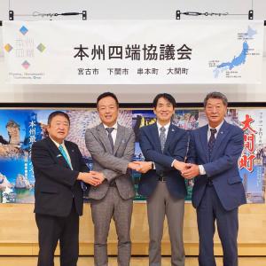 「本州四端協議会」と書かれた横断幕の下にポスターが貼られた前で、市長と男性3名が隣の人と握手するように腕を交差させ、並んで撮影した写真