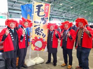 宮古市魚市場の「毛ガニ祭り」の旗の周りで頭に毛ガニの被り物をしてお揃いの法被をきた男性5名がピースをしながら記念撮影をしている写真