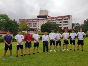 芝生の広場で市長が中央に立ち、両手を前に組んだ学生立ち9名が横一列に並んでいる写真