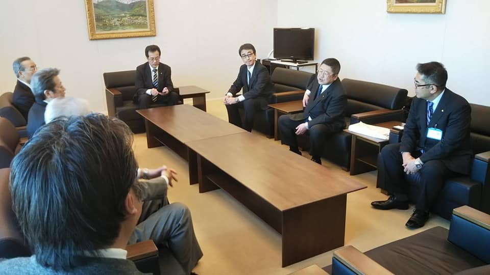 挨拶に訪れた川崎近海汽船株式会社の応接室内で、石井繁礼代表取締役会長他3名のご担当者と市長と副市長、関係者の男性が2つの茶色のテーブルを囲んで座り話をしている様子の写真