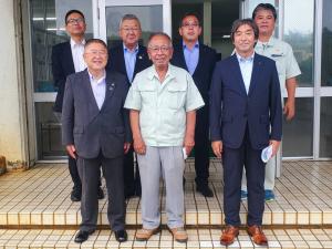 建物の入り口で、宮古製糖の渡久山社長を中央に市長や4名の関係者、1名の従業員の方が2列に並んでいる記念写真