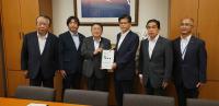 壁に額に入った大きな絵画が飾られた室内で、公明党の石井啓一幹事長と市長が要望書を一緒に持ち、若松謙維参議院議員と宮古市議会の橋本久夫議長、宮古商工会議所の大坂文人副会頭と2名の関係者が横一列に並んでいる写真