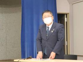 説明会の会場で市長が資料とマイクが置かれた自席に立っている写真