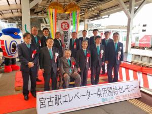 宮古駅ホームを紅白幕で飾りくす玉が割られ「宮古駅エレベーター供用開始セレモニー」の関係者の方々が白色と赤色の胸章リボンをつけながら記念撮影をしている写真