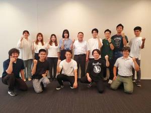 前列に膝立ちで5名、後列に市長を中心に9名が立って並び、全員が片腕を曲げ握りこぶしを顔の横に掲げてポーズを決めて写っている記念写真