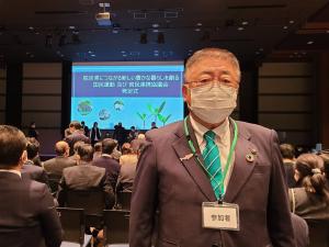 画面が映し出されたスクリーンと椅子に座る参加者たちに背を向けて正面を見る市長を写した写真