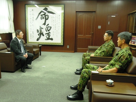 応接室の部屋で、向かい合わせに市長と迷彩服を着た自衛隊員2名が椅子に座って会話している様子の写真