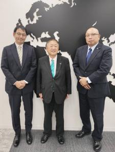 白黒の地図のようなものが書かれた壁の前で、スーツを着た市長と2名の男性が並んでいる写真
