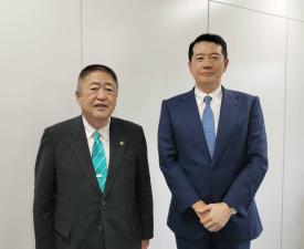 白い壁の前で黒色のスーツを着た市長と、紺色のスーツを着た男性が並んでいる写真