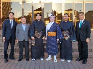 市長と副市長が衣装を着た若手琉球芸能家である高井賢太郎さん、棚原健太さん、町田倫士さんの3人と関係者1人と建物入口で並んで撮影した写真