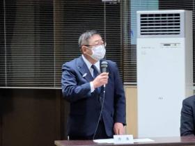 説明会の会場で「市長」と書かれたネームプレートが置かれたテーブルの前に立ちマイクを片手に持ちながら市民の方に説明をしている写真