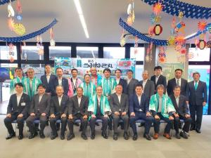 スーツや法被を着た関係者の方々が2列に並んでいる集合写真