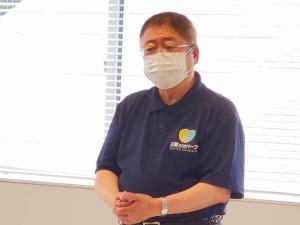 ブラインドが掛けられた窓を背にして、両手をお腹の前で組みマスクをして話している様子の市長の写真
