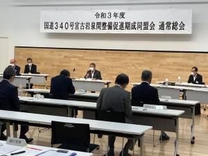 「令和3年度国道340号宮古岩泉間整備促進期成同盟会 通常総会」と書かれた横断幕の下で席に着き話をしている様子の市長の写真