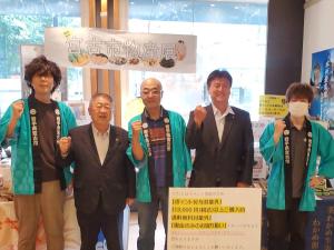 青い法被を着た男性3人と、スーツを着た市長と関係者の男性が横一列に並ぶ記念写真