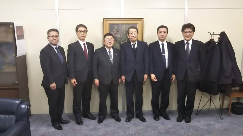 大きな額に入った絵画が壁に設置された室内で、ラサ工業株式会社の庄司宇秀取締役社長と坂尾事業部長と仲総務部長、市長と副市長と関係者の男性が横一列に並んでいる写真