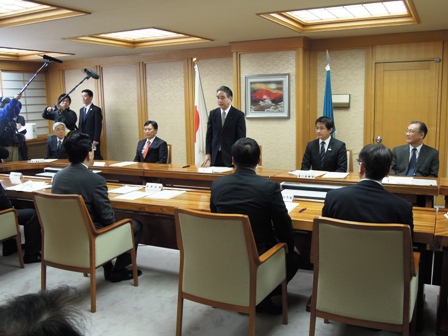 向かい合って設置された長机の中央にスーツの男性が立ち話している意見交換会の写真