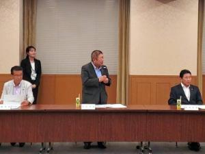 市長が長机の自席で立ち、マイクを持ち、話をしている写真