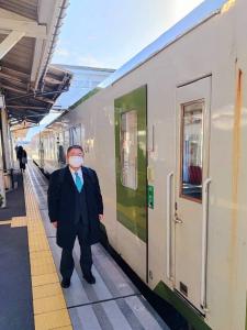 駅のホームで市長が黄色い点字線と電車の間に立ち記念撮影をしている写真
